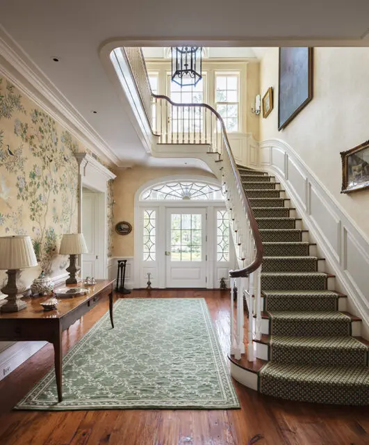 Foyer with floral wallpaper, curved staircase, and green patterned runner