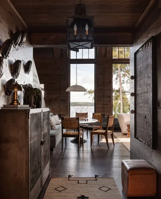 Dining area with round table, woven chairs, and lake view through large windows.