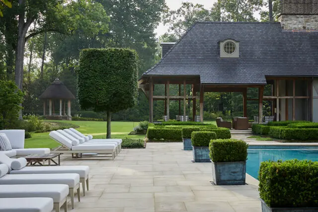 Stone patio with lounge chairs, pool, and manicured hedges