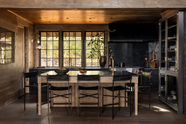 Kitchen with wood ceiling, black marble backsplash, and island with black stools.