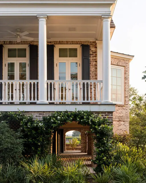 Brick home with white columns, balcony, and arched walkway covered in vines.