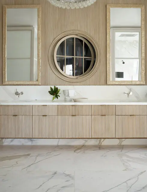 Master bathroom with fluted wood vanity, marble countertops, and round closet window.