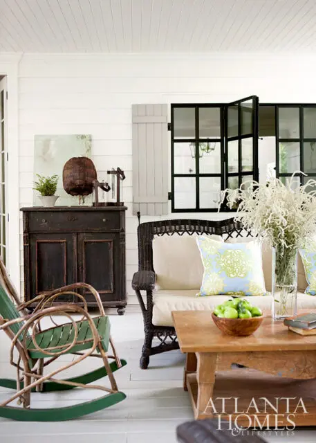 Porch with wicker sofa, rocking chair, dark cabinet, and coffee table with apples