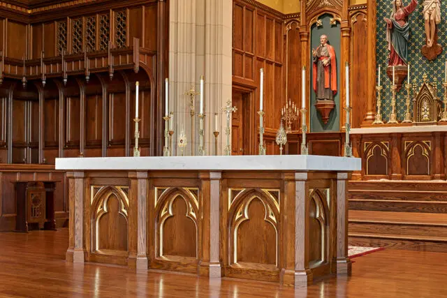 Church altar with marble top and ornate wooden base, featuring brass candlesticks and religious