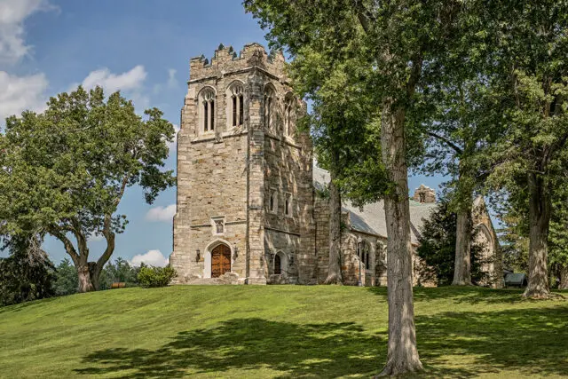 Stone church with Gothic architecture, arched doorways, and crenellated tower on a grassy hill.