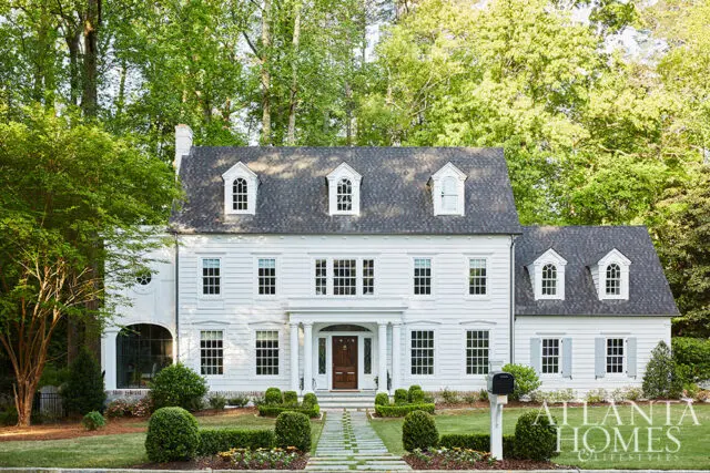 White colonial house with dormer windows, symmetrical facade, and manicured lawn.