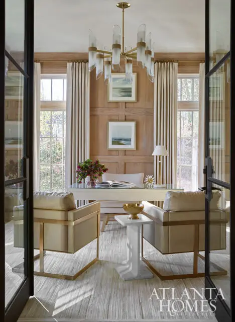 Office with wood paneled walls, two tan armchairs, and a glass-top desk.