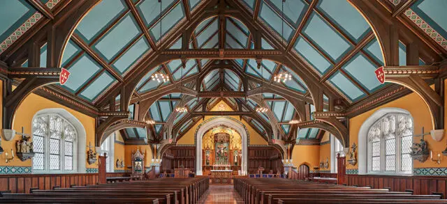 Church interior with wooden pews, ornate wooden ceiling beams, and stained glass windows.