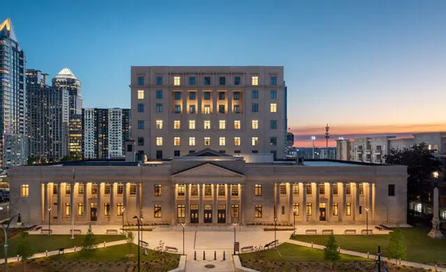 Classical building with columns and a modern high-rise in the background at dusk.