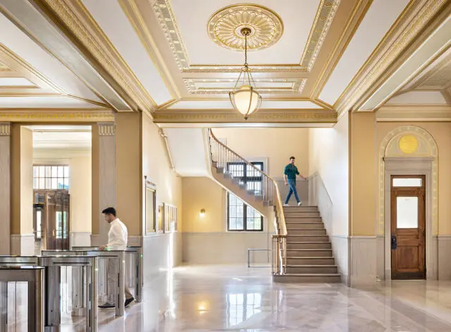Lobby with ornate gold and white ceiling, marble floors, and a grand staircase.