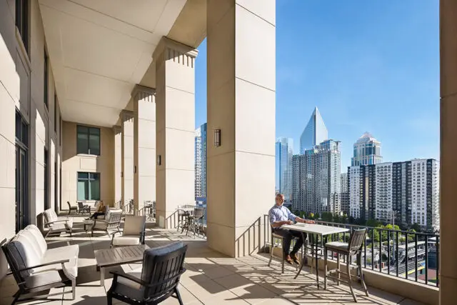 Balcony with seating and city skyline view. Man sits at table.