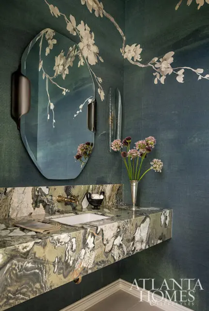 Powder room with green floral wallpaper, marble vanity, brass faucet, and unique mirror.
