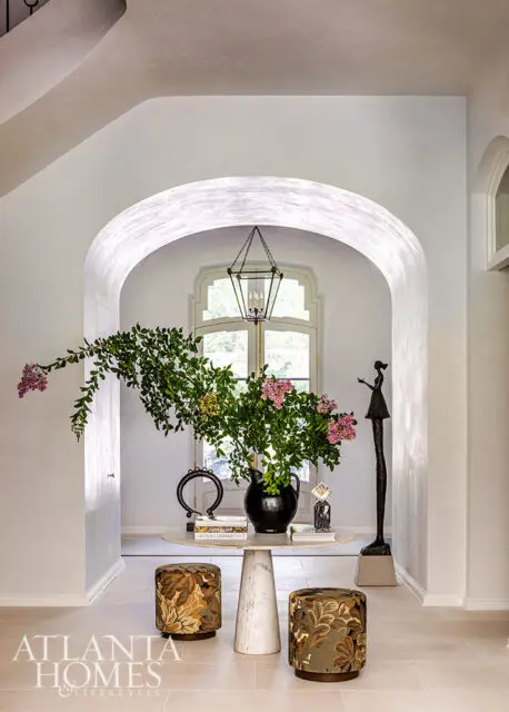 Entryway with arched doorway, marble table with floral arrangement, two patterned ottomans, and a