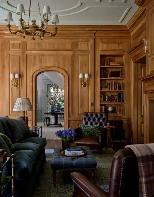 Library with wood paneled walls, tufted leather armchair, and dark blue sofa.