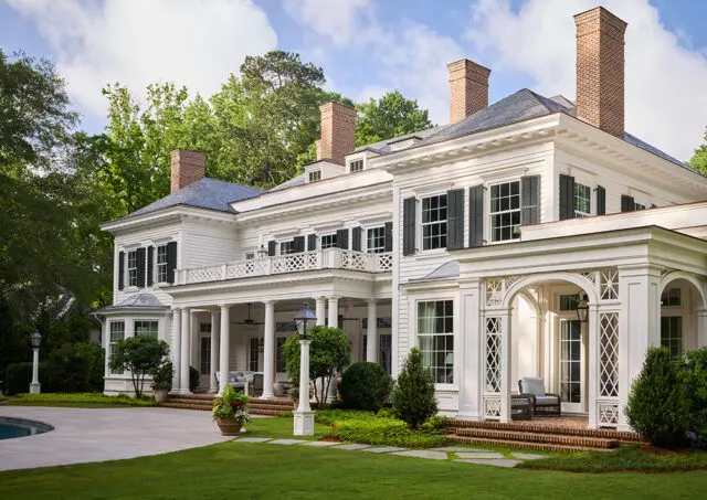 White country house with columns, shutters, brick chimneys, and a balcony.