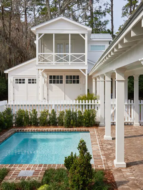 White house with screened porch, garage doors, and a brick patio with a pool.