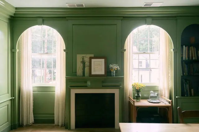 Green paneled room with arched windows, fireplace, and built-in bookshelves.