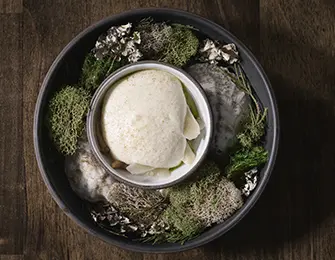 Creamy mousse served in a bowl surrounded by moss and decorative elements