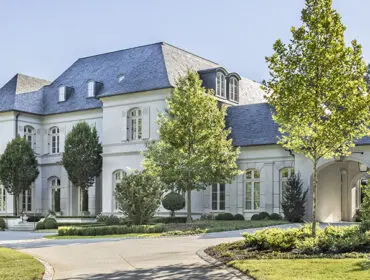 White mansion with gray slate roof, dormer windows, and manicured landscaping.