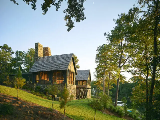 Stone and wood cabin with screened porches on a grassy hill overlooking a lake