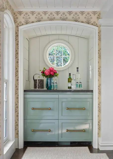 Mint green cabinets with brass hardware, dark countertop, and a round window above