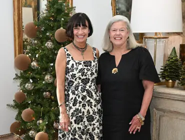 Two women pose in front of a decorated Christmas tree.