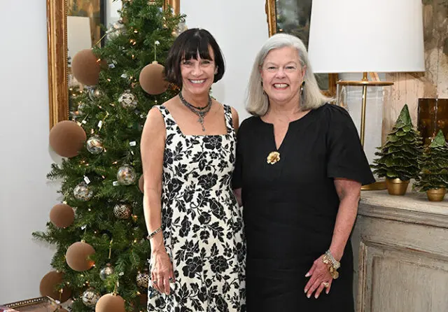 Two women pose in front of a decorated Christmas tree.