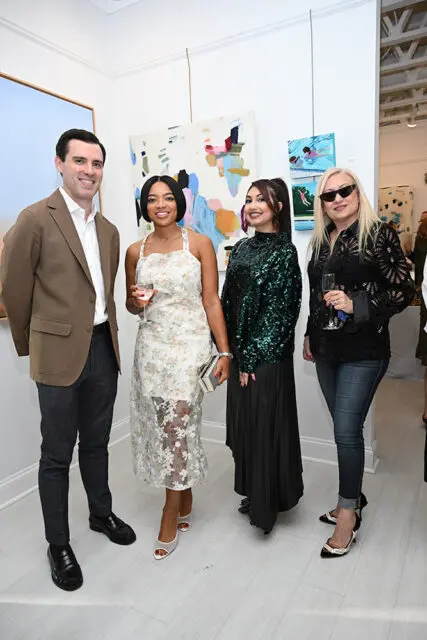 Four people posing in front of abstract art at an event.