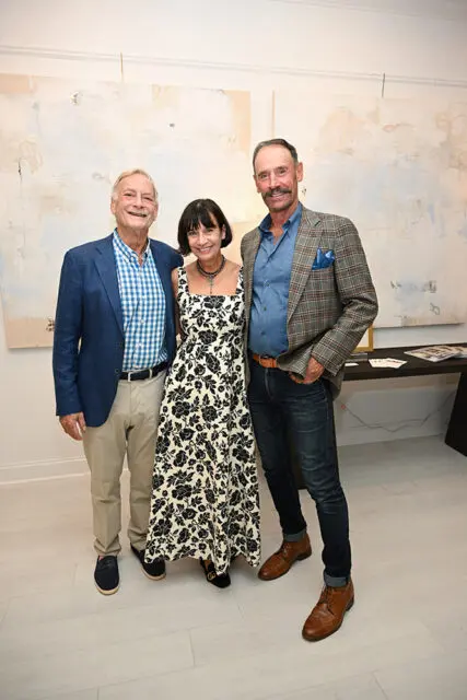 Three people pose in front of abstract art. Man on left wears blue checkered shirt and blazer
