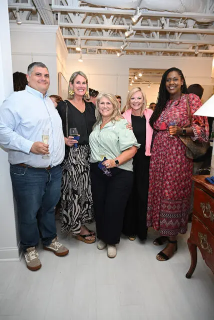 Five people posing for a photo at an event. The woman on the far left holds a champagne flute.