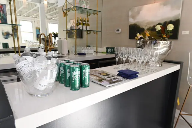 White bar with bottles of water, cans of Perrier, champagne flutes, and a silver ice bucket.