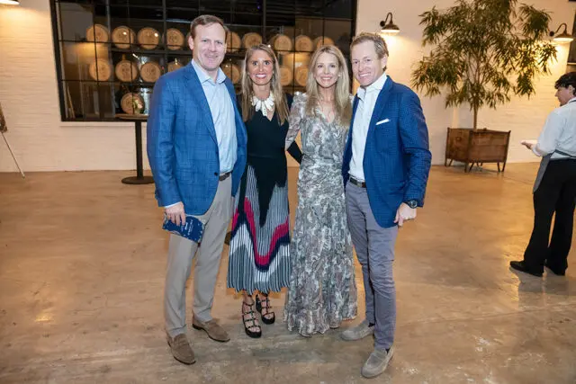 Four people posing indoors with barrels in the background.