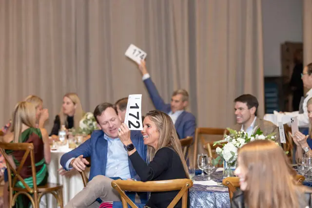 Woman holding paddle 172 at auction event. Man holds paddle 174.
