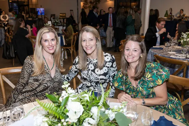 Three women smiling at a table with a floral centerpiece.