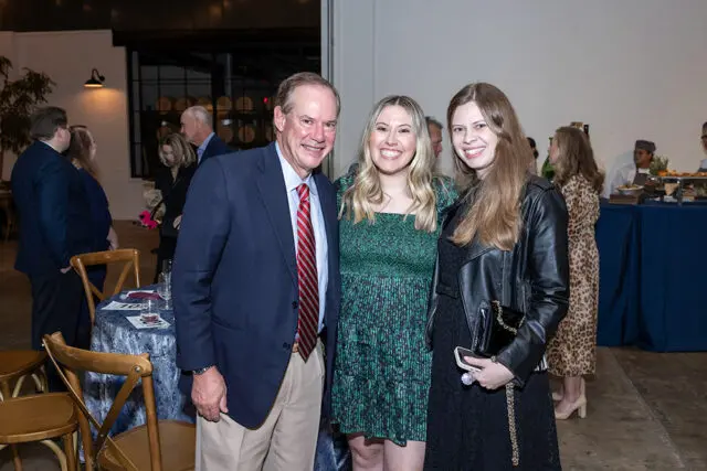 Man in navy suit and red striped tie with two women, one in green dress, one in black dress and