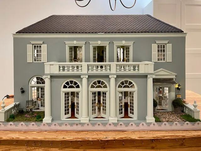 Gray dollhouse with white trim, shutters, balcony, and arched French doors.