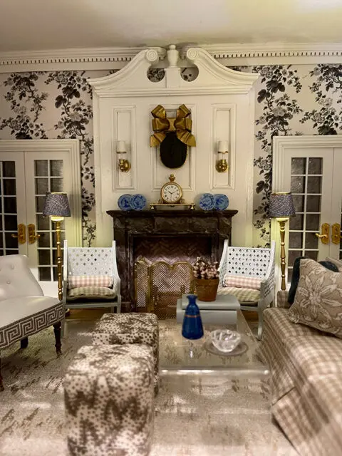 Dollhouse living room with floral wallpaper, fireplace, and miniature furniture.