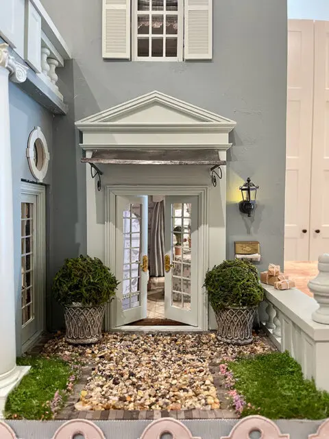Dollhouse entryway with double doors, planters, and gravel path.