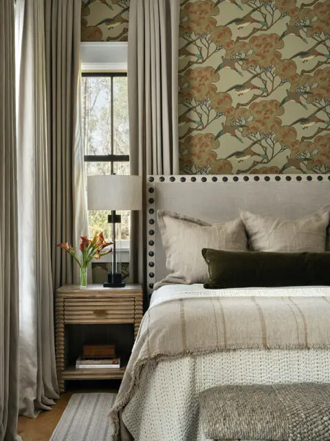 Bedroom with patterned wallpaper, upholstered headboard, and neutral bedding.