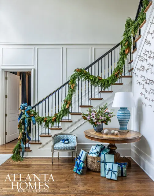 Staircase decorated with Christmas garland, blue gifts, and a floral arrangement.