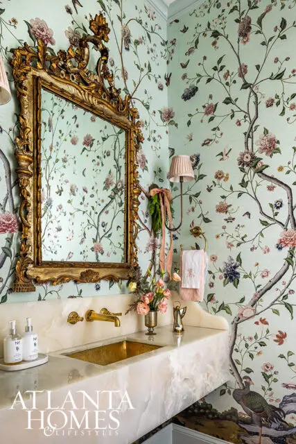 Powder room with floral wallpaper, ornate gold mirror, and marble vanity with brass sink.