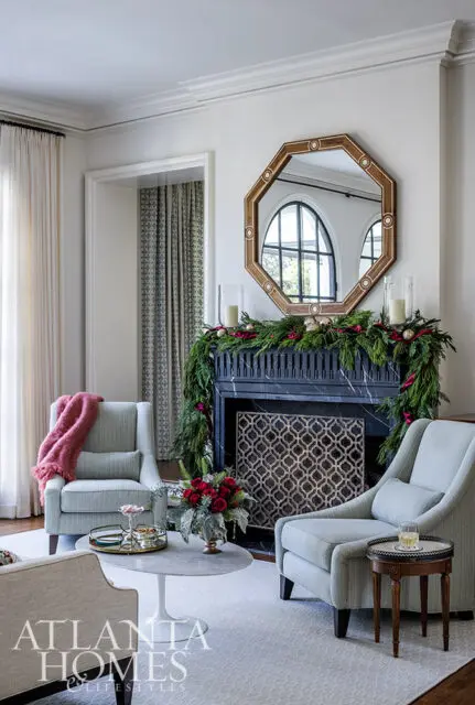 Living room with light blue armchairs, marble coffee table, and fireplace decorated for Christmas.