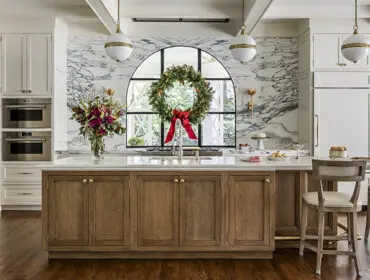 Kitchen island with wood cabinets and marble countertop, featuring a wreath on arched window.