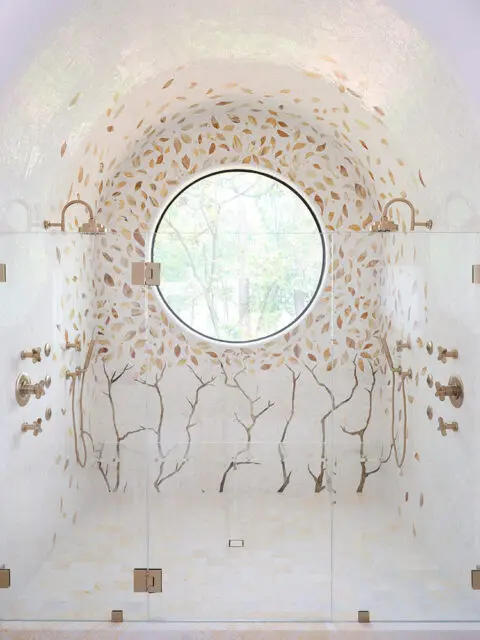 Shower with mosaic tile walls featuring a leaf pattern and tree branches, and a circular window.
