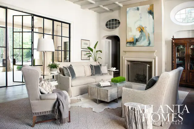 Living room with neutral sofa, wingback chair, abstract art above fireplace, and large glass doors