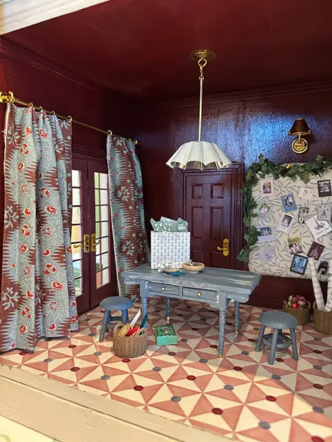 Dollhouse room with patterned curtains, a blue desk, and a geometric tile floor.