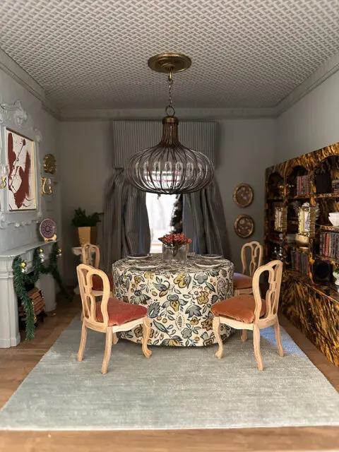 Dining room with floral tablecloth, light blue rug, and ornate chairs.