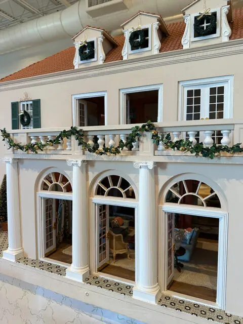 Dollhouse facade with arched doorways, columns, and a balcony decorated with garland.
