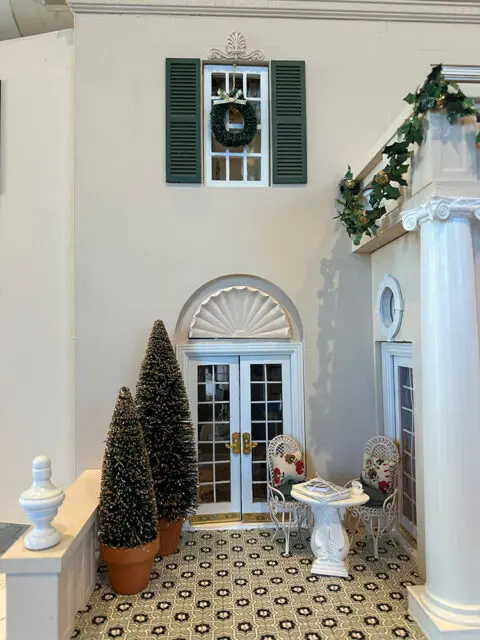 Dollhouse patio with French doors, two chairs, a table, and two potted trees.