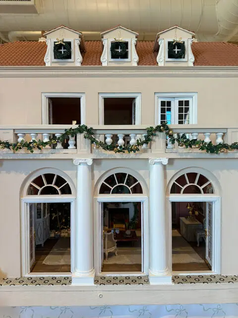 Dollhouse facade with arched doorways revealing decorated rooms and a balcony with garland